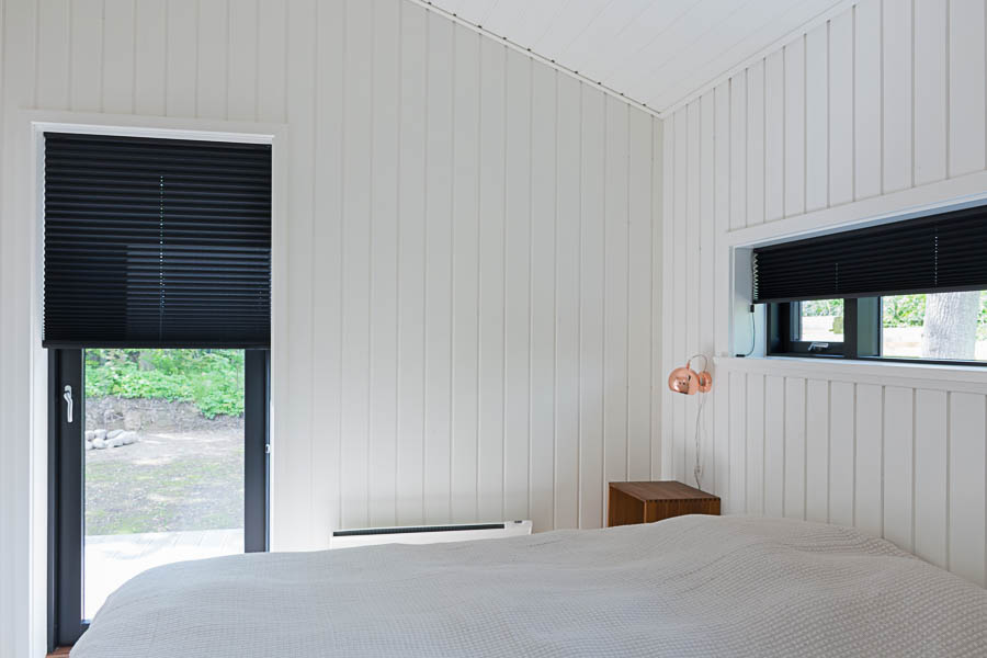 Soveværelse med sorte plisegardiner skaber flot kontrast i det lyse rum.